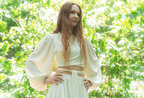 Red-haired woman in white standing with hands on hips outdoors.