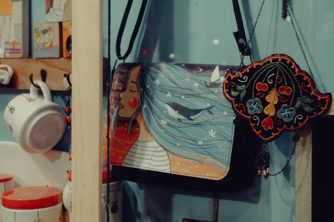 Illustrated handbag with woman and whale, beside an embroidered decoration